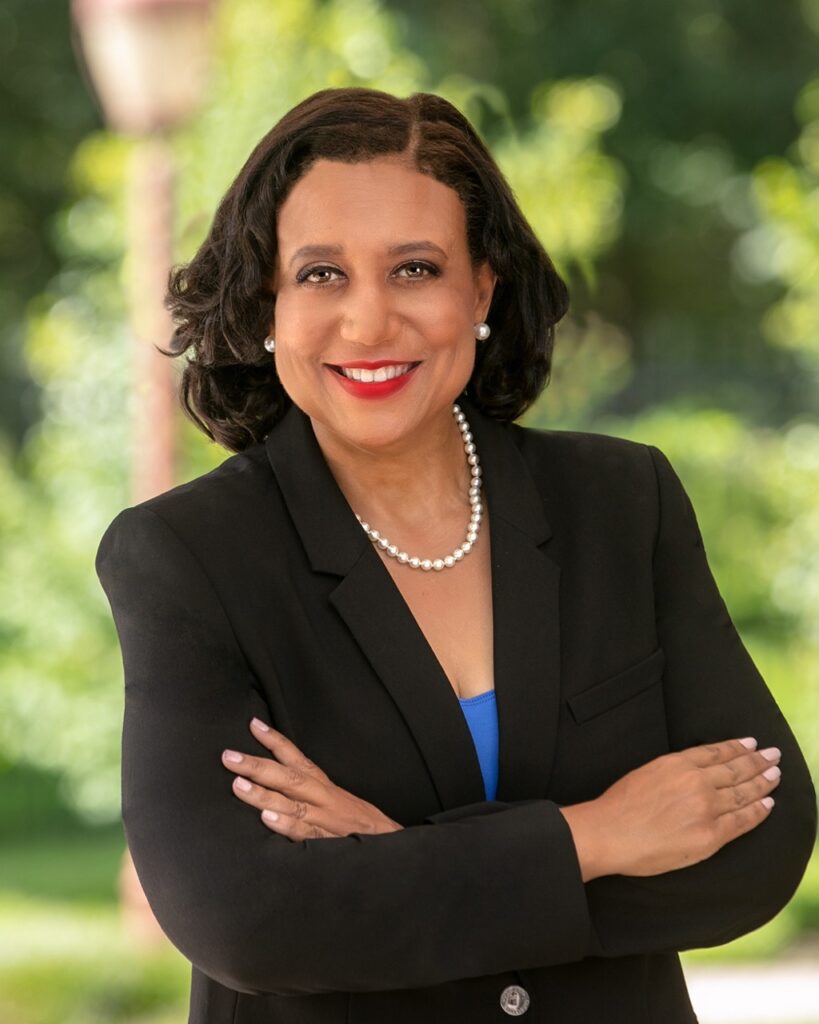 Smiling woman in black blazer, outdoor background.